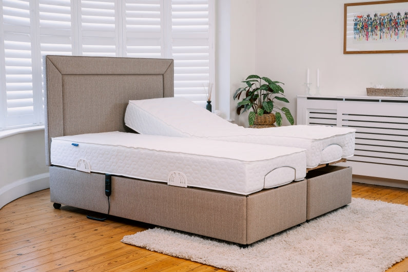Twin adjustable bed with beige upholstered base and matching headboard, showing one mattress flat and the other raised.