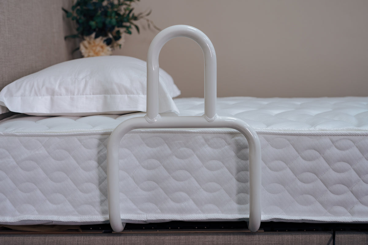White adjustable bed rail on a bed with white bedding and pillows.