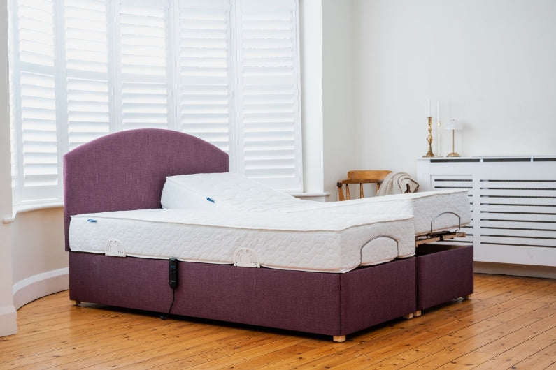Twin adjustable bed with purple upholstery and curved headboard, showing one mattress flat and the other raised.