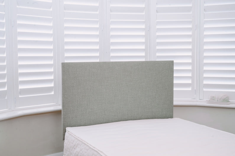 Gray upholstered headboard against a window with white blinds