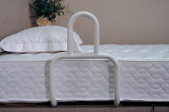 White adjustable bed rail on a bed with white bedding and pillows.