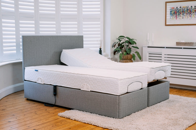 Gray adjustable bed frame with white mattress in a room with wooden flooring and a plant.