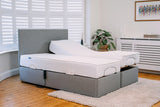 Gray adjustable bed frame with white mattress in a room with wooden flooring and a plant.