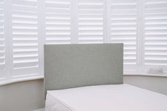 Gray upholstered headboard against a window with white blinds