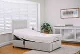 White adjustable bed with storage drawers in a room with wooden flooring and a plant.